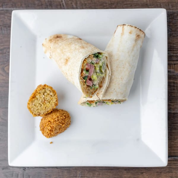 Two falafel wraps with fresh vegetables and two falafel balls on a white square plate.