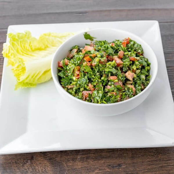 A white bowl of Lazeez Fresh Mediterranean Grill's tabbouleh salad with lettuce on a white plate.