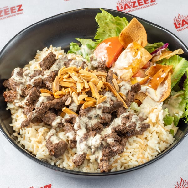 A black bowl filled with rice, meat, almonds, lettuce, tomatoes, and pita bread, drizzled with sauce.