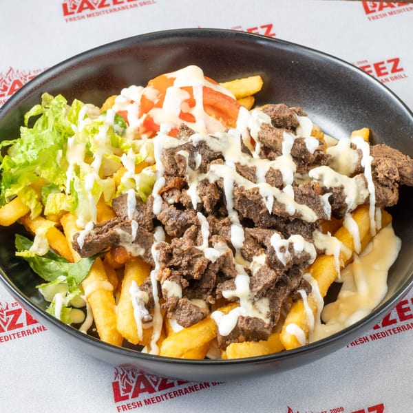 A black bowl of Lazeez fries topped with beef shawarma, lettuce, tomatoes, and white sauce.