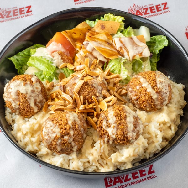 A bowl of rice topped with falafel, almonds, and a fresh salad with dressing.