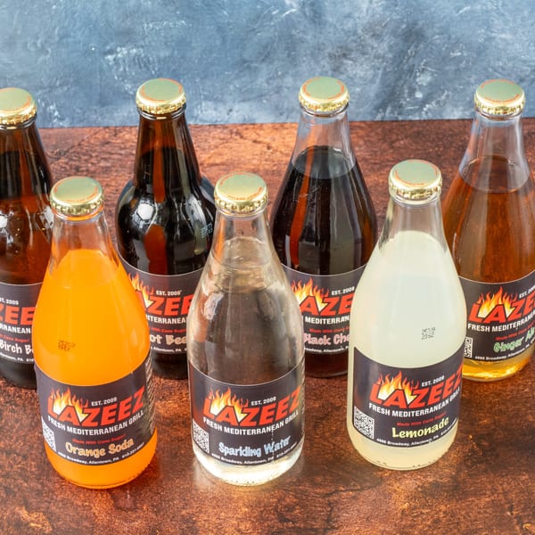 Six bottles of Lazeez Fresh Mediterranean Grill sodas and sparkling water on a wooden surface.